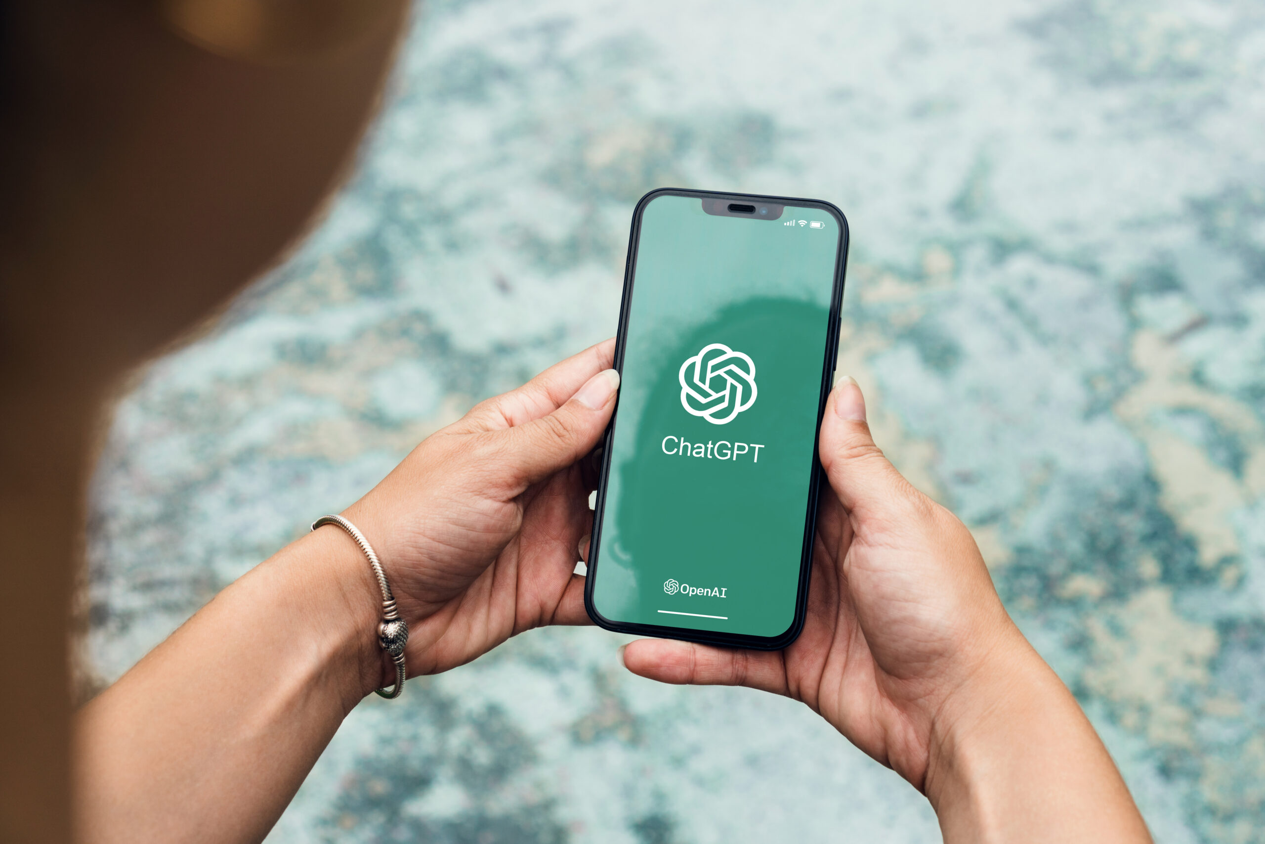 Picture of hands holding a mobile phone displaying ChatGPT logo