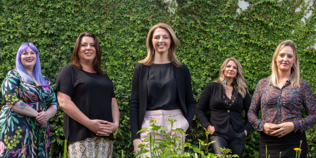 Five members of the Content Empire team posting in front of an ivy covered wall.