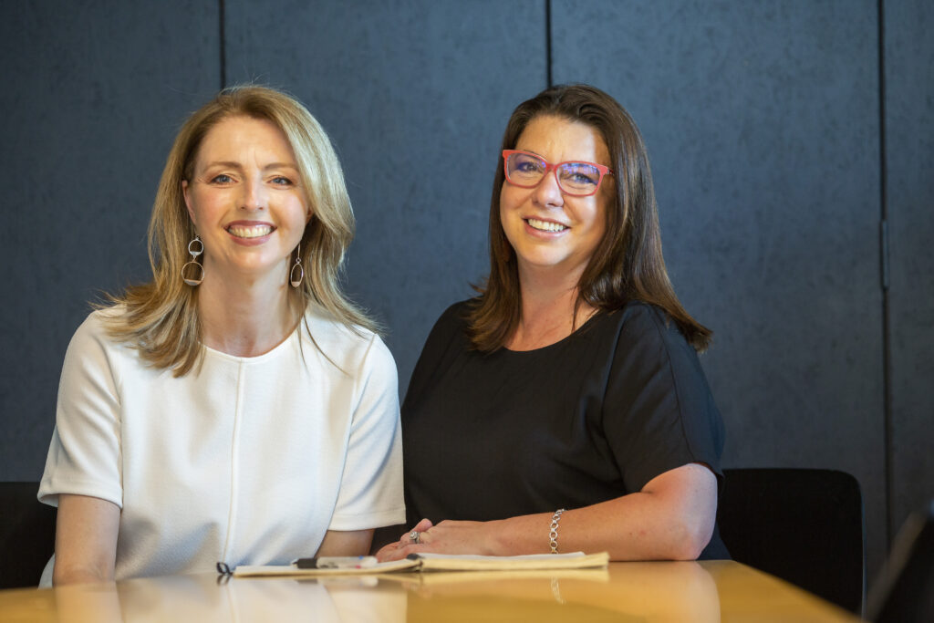 Content Empire founders, Cathy Wever and Clare Murphy seated at a table smiling at the camera.